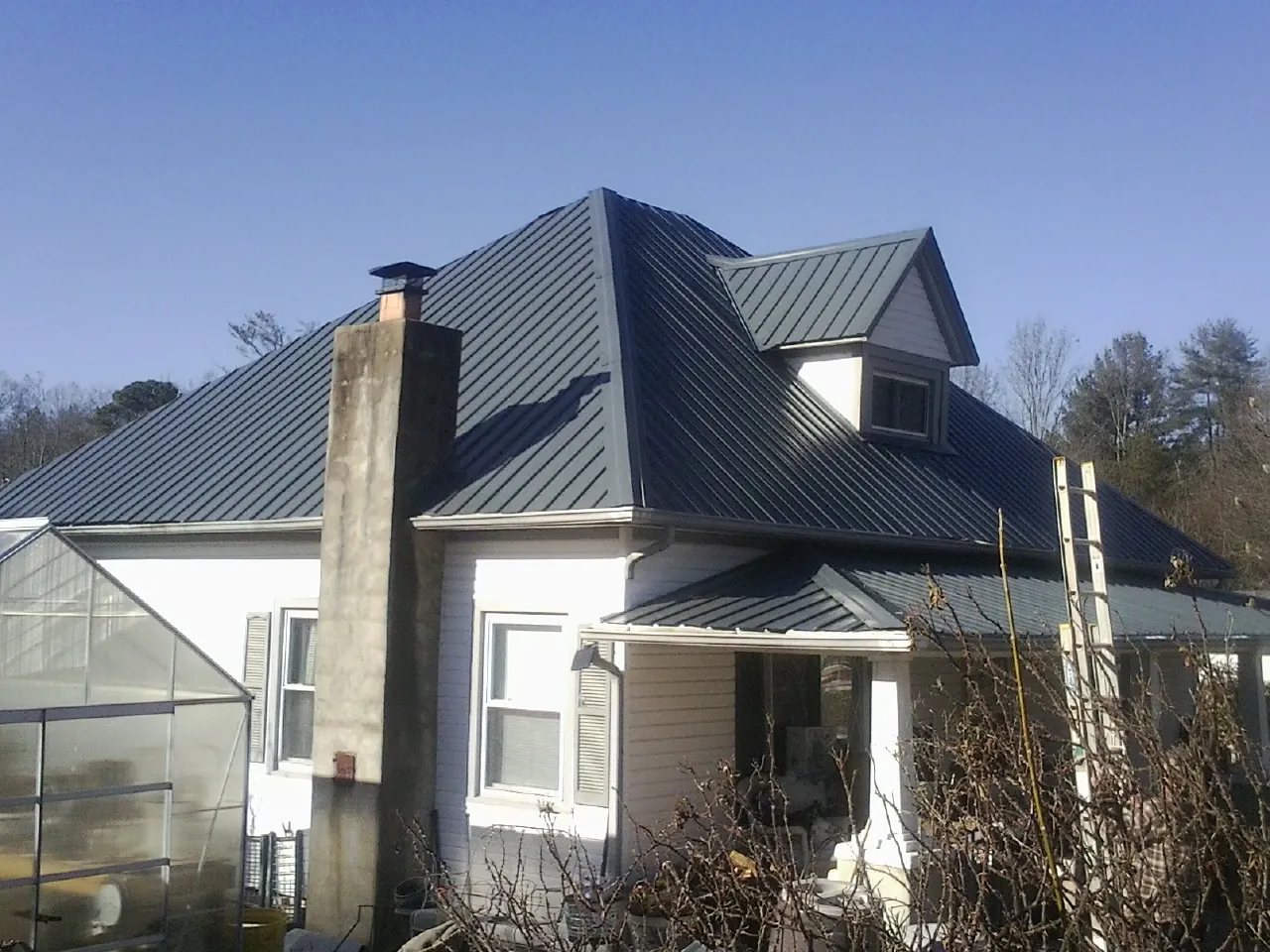 Dark blue standing seam metal roof on a white farmhouse with dormer — Slate & Tile Roof Repair by Roofing Brothers in Sharon Center