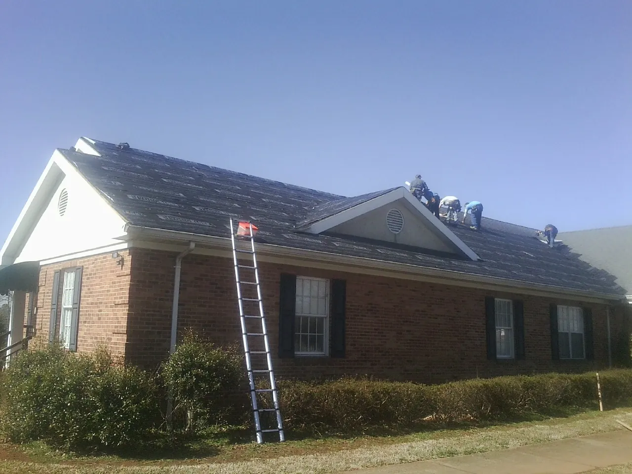 Crew tearing shingles off a brick ranch roof with a ladder set — Metal Roof Repair work by our crew in Sharon Center