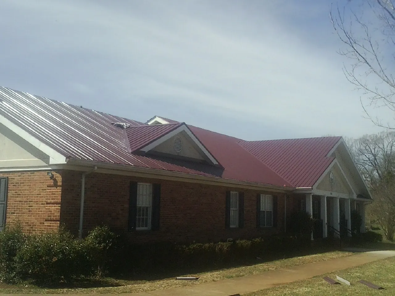 Red metal roof with gabled entries on a long brick building, from a Hail Damage Roof Repair job in Sharon Center