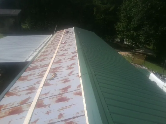 Old rusted panels beside newly installed green metal roofing — Wind Damage Roof Repair by Roofing Brothers in Sharon Center