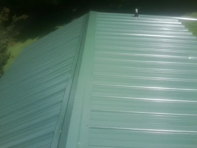 New green metal panels meeting at the ridge of a roof — Flat Roof Repair work by our crew in Sharon Center