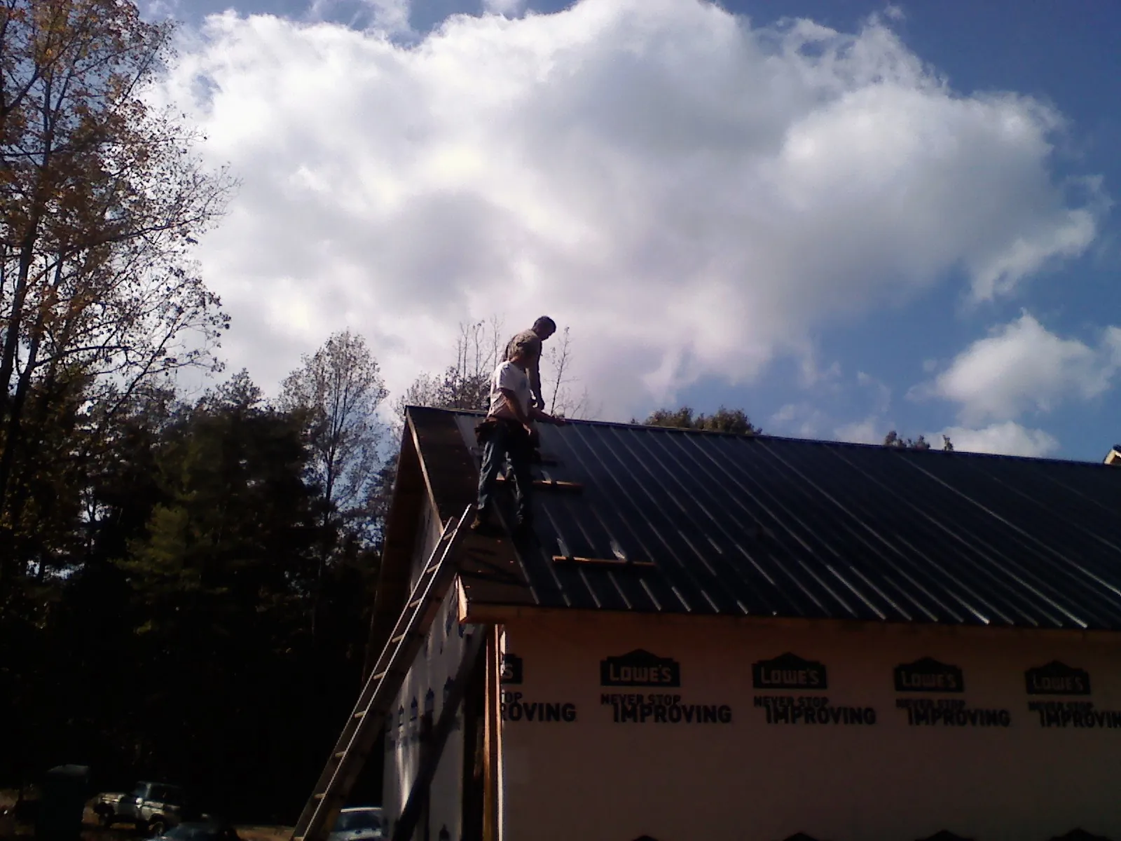 Roofer fastening dark metal panels high against a cloudy sky, from a Roof Inspection job in Sharon Center