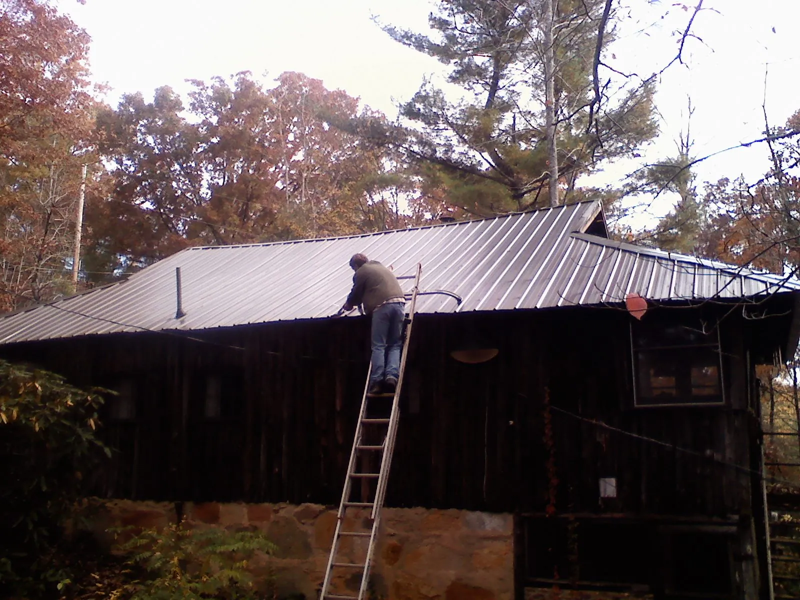 Roofer on a ladder working along the edge of a cabin metal roof in Sharon Center