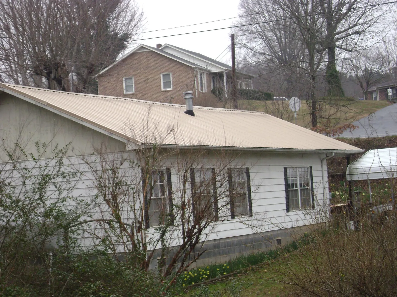 Tan metal roof on a white sided house set into a hillside — Commercial Roofing by Roofing Brothers in Sharon Center