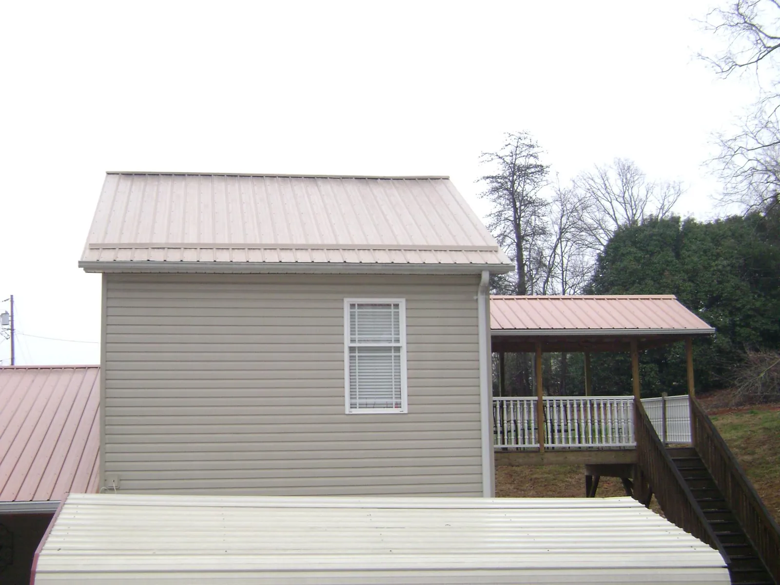 Tan metal roofs on a two story addition and attached porch, from a Roof Replacement job in Sharon Center